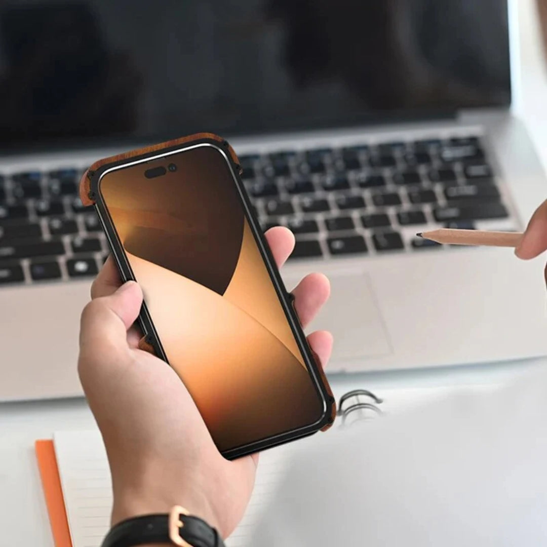 A person holds an iPhone case in a rugged, wood edged apple cover with a metallic frame, shown against a laptop setup for iphone 15 pro max cover