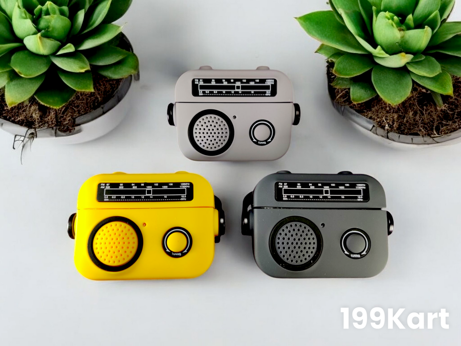 A set of three radio style airpods pro 2 case in yellow, dark grey, and light grey placed between potted plants on a white surface.