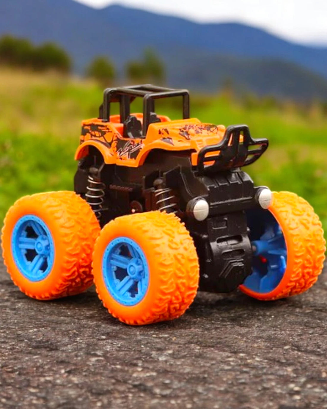 Orange and black monster truck toy with blue wheels placed outdoors, emphasizing bold design and sturdy build