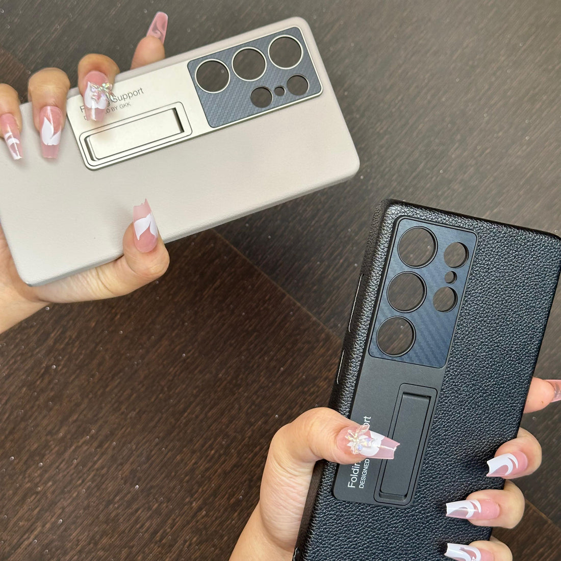 Close up of hands holding beige and black Samsung covers with metallic ring kickstands and textured leather finish for S25 Ultra