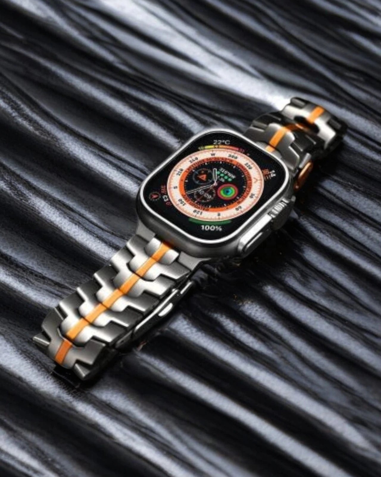 Stylish apple watch straps with a silver and orange titanium band resting on a textured black surface 